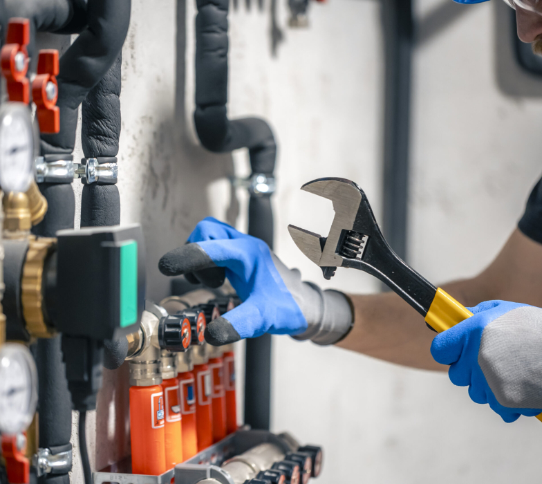 A man installs a heating system in a house and checks the pipes with a wrench. Adjusting heating valves in a residential building. A plumbing and heating technician works.
